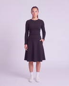A woman  modeling a lightweight athletic black flared skirt with side pockets, paired with white socks and white sneakers