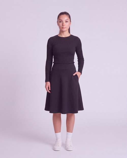 A woman  modeling a lightweight athletic black flared skirt with side pockets, paired with white socks and white sneakers