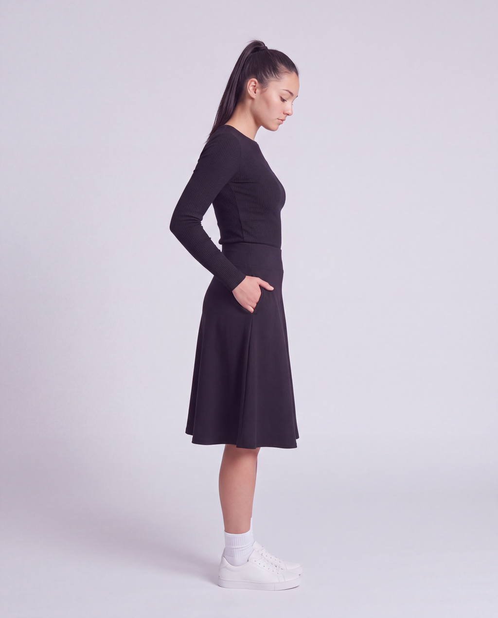 A woman side profile modeling a lightweight athletic black flared skirt with side pockets, paired with white socks and white sneakers