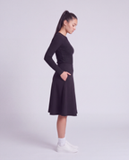 A woman side profile modeling a lightweight athletic black flared skirt with side pockets, paired with white socks and white sneakers