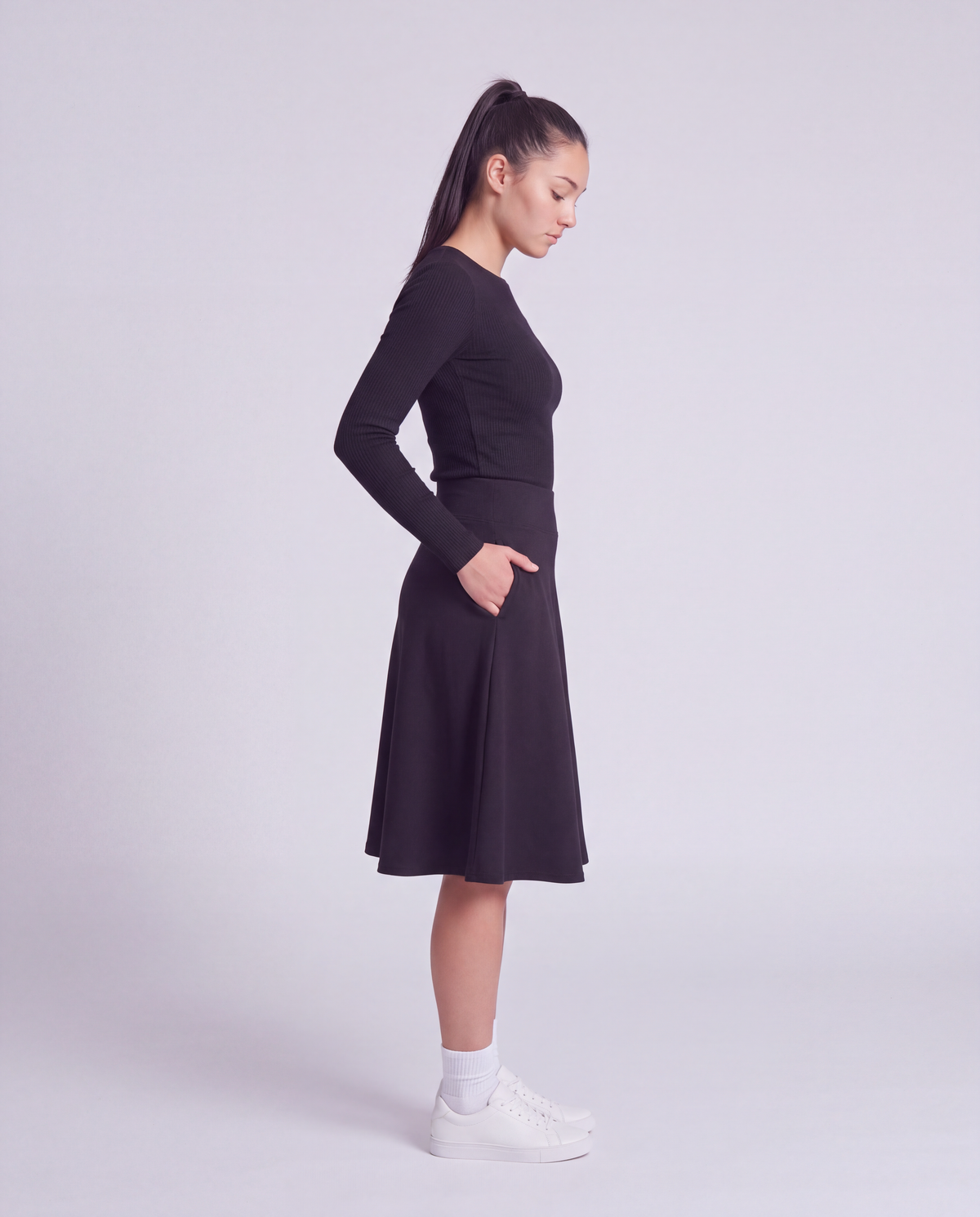 A woman side profile modeling a lightweight athletic black flared skirt with side pockets, paired with white socks and white sneakers