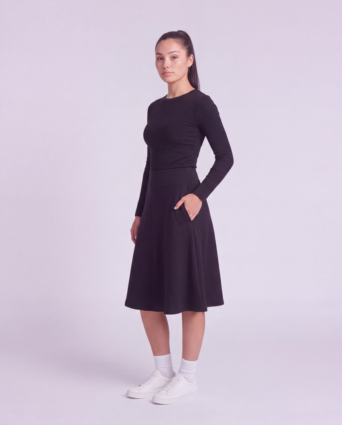 A woman modeling a lightweight athletic black flared skirt and side pockets, paired with white socks and white sneakers