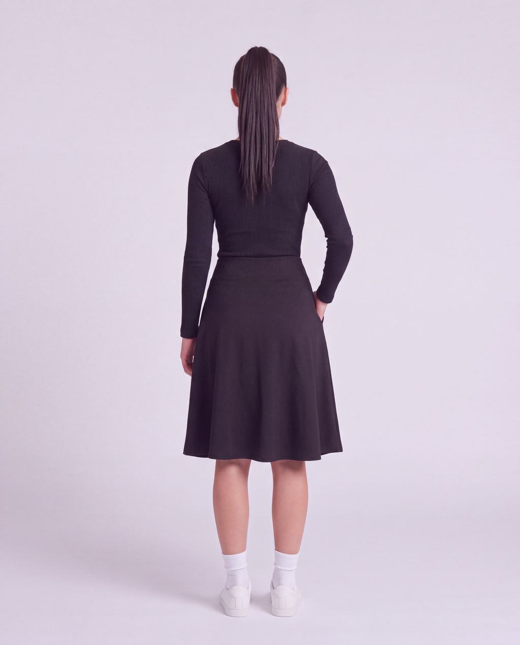 A woman back modeling a lightweight athletic black flared skirt with side pockets, paired with white socks and white sneakers