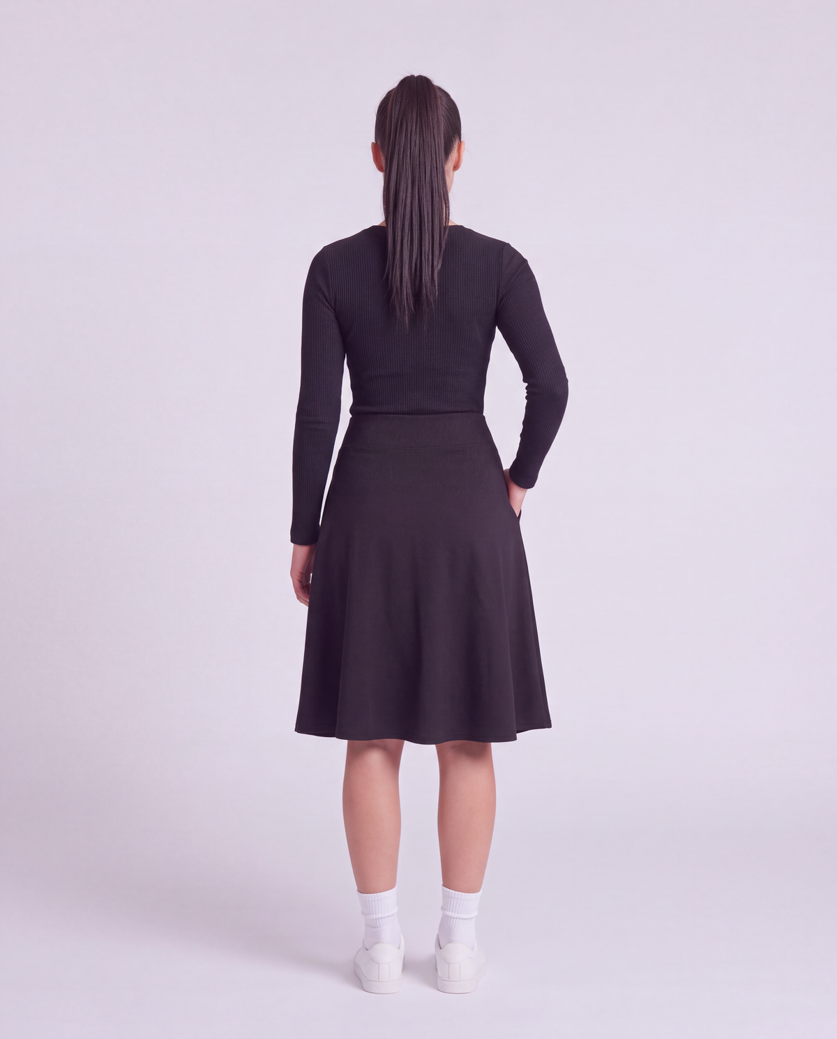 A woman back modeling a lightweight athletic black flared skirt with side pockets, paired with white socks and white sneakers